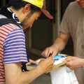 劇場前で映画のチラシにサインするなすびさん